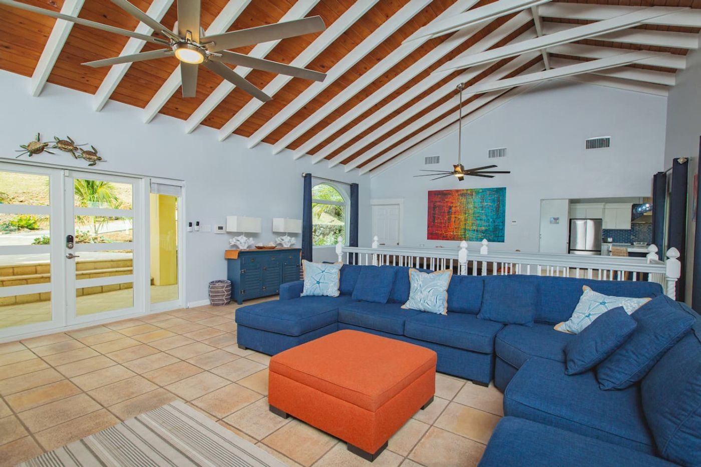 Living room with a vaulted beamed ceiling, a blue sectional sofa, an orange ottoman and French doors to the veranda