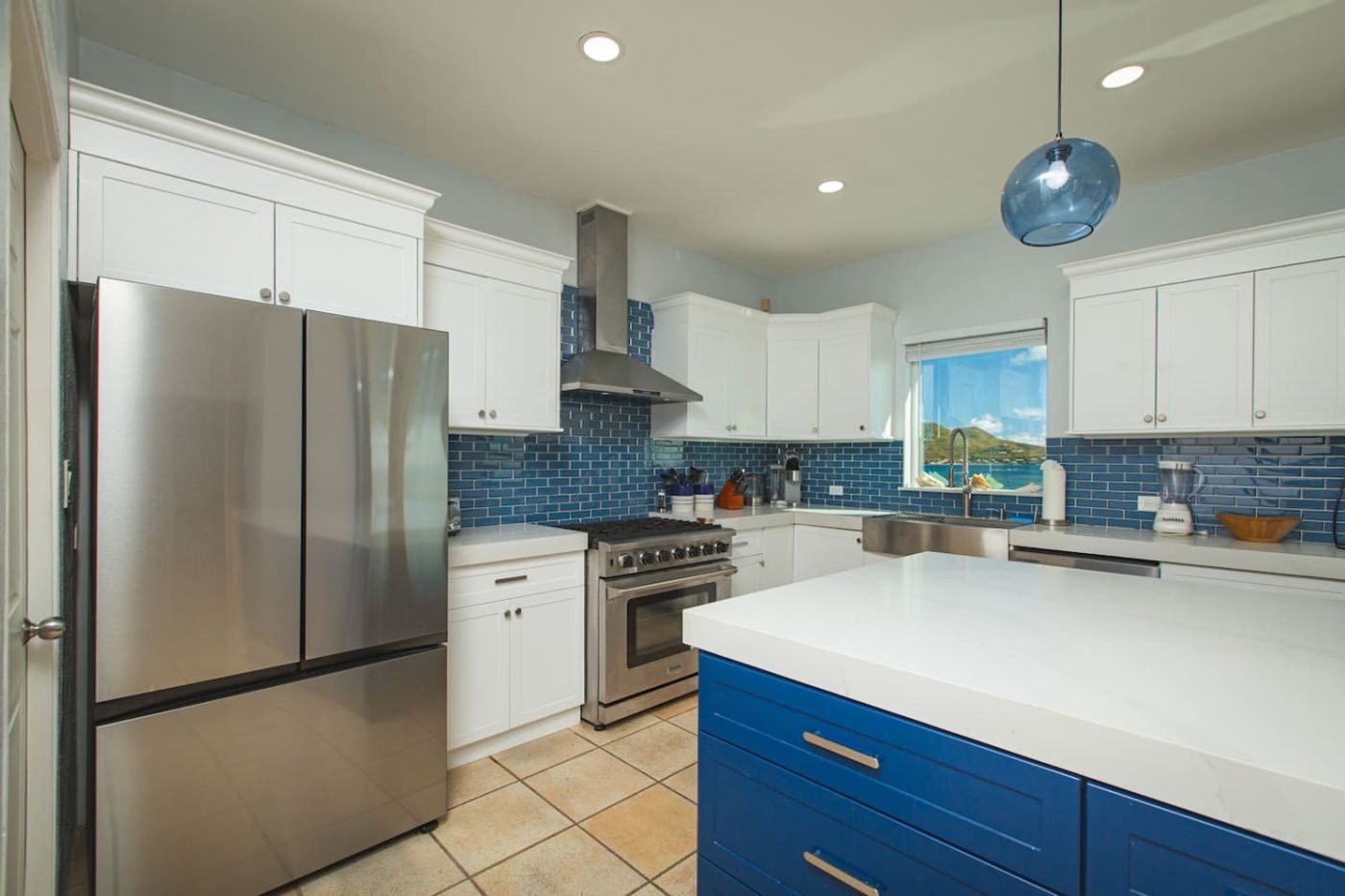 Kitchen with white cabinets, a blue island, stainless steel appliances and a window over the sea