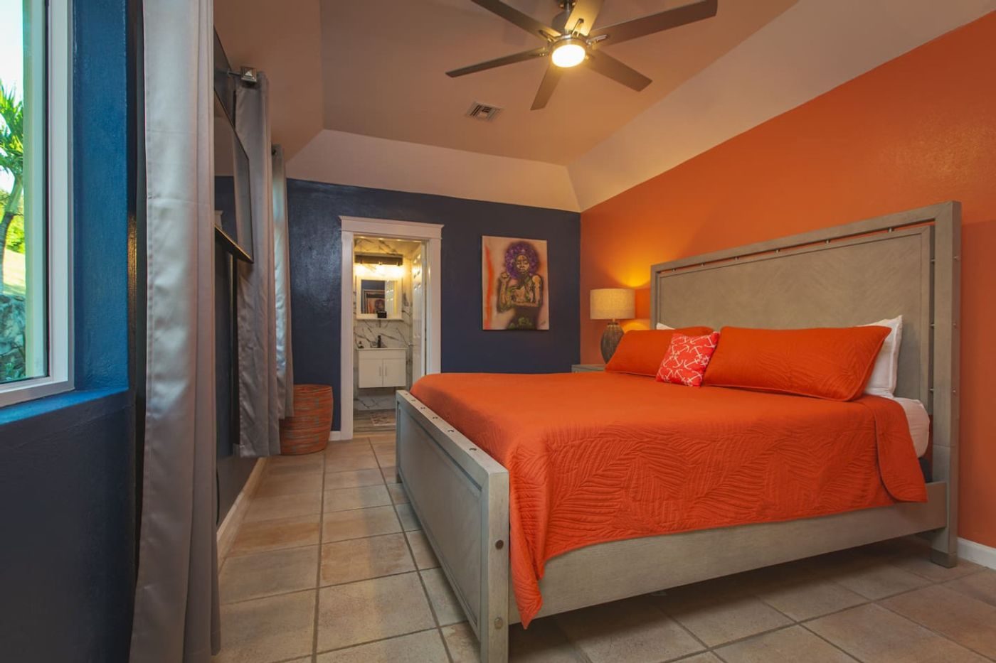 Bedroom with an orange accent wall, an orange-covered bed and a doorway through to an en-suite bathroom