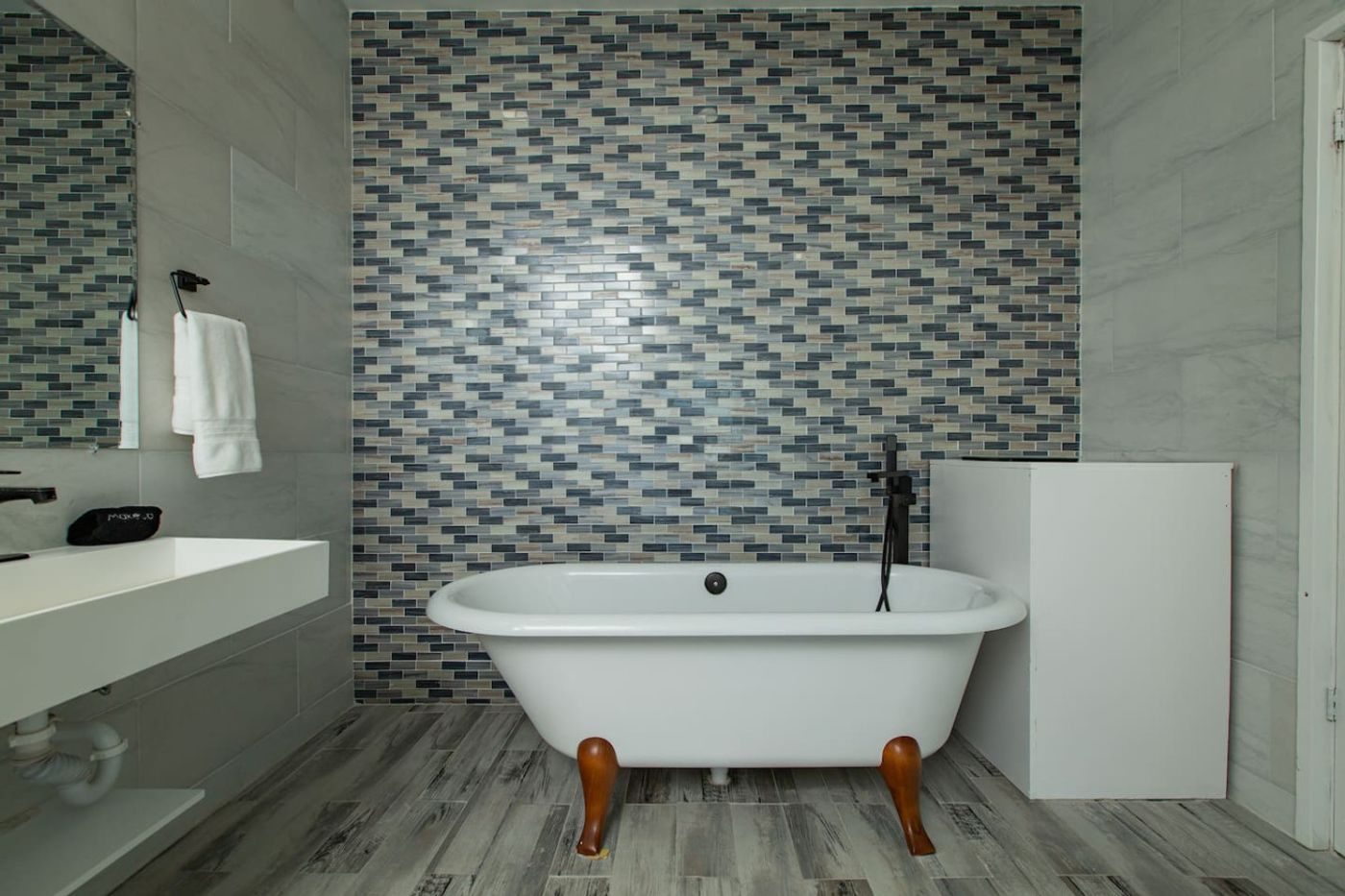 Freestanding clawfoot bathtub against a mosaic tile wall