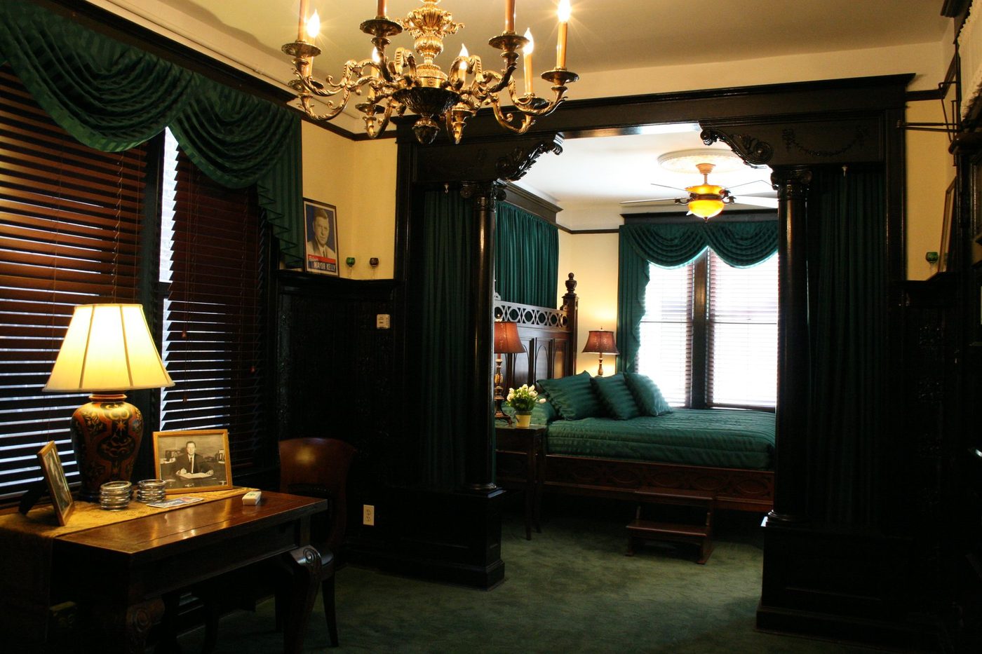 A dark wood four-poster bed beneath a brass chandelier in the Mayors' Suite at The Polo Inn, Chicago