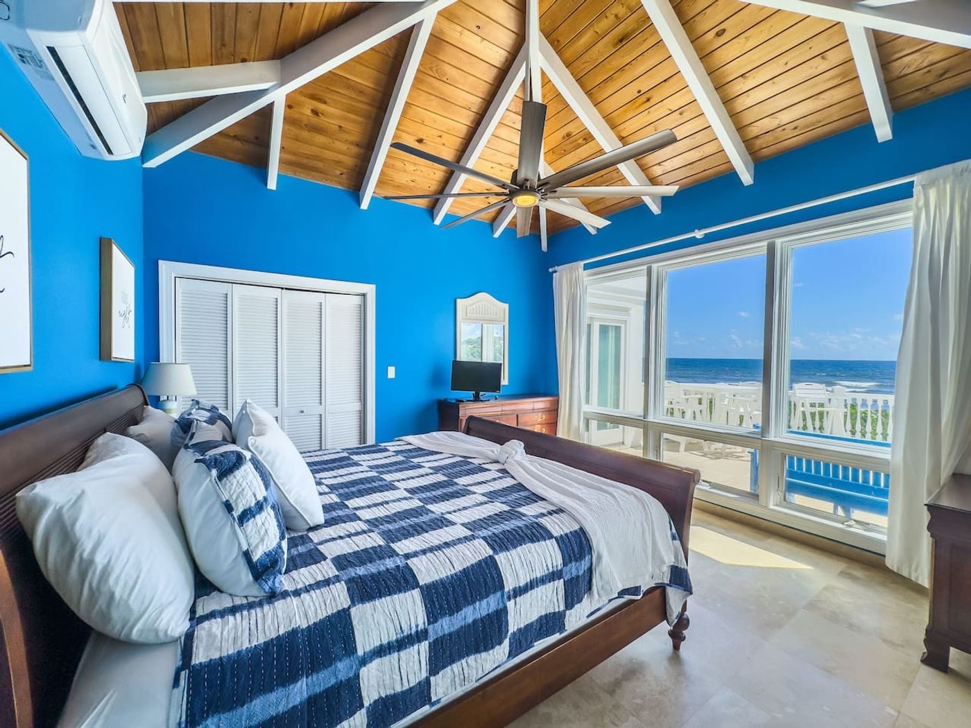 Bedroom with bright blue walls, a navy and white quilt and a wall of windows facing the sea