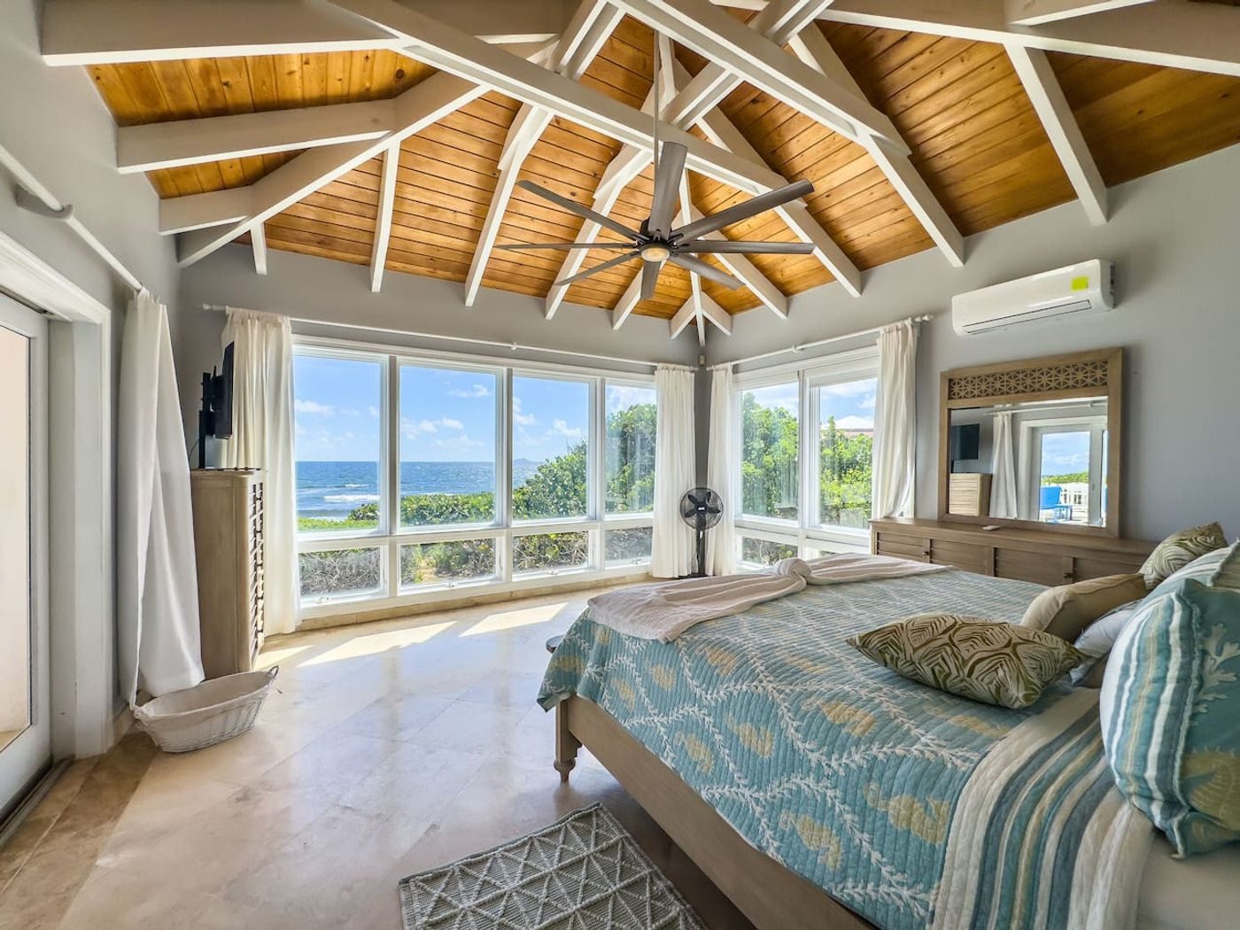 Bedroom under a pitched wood ceiling with a wall of windows looking straight out at the sea