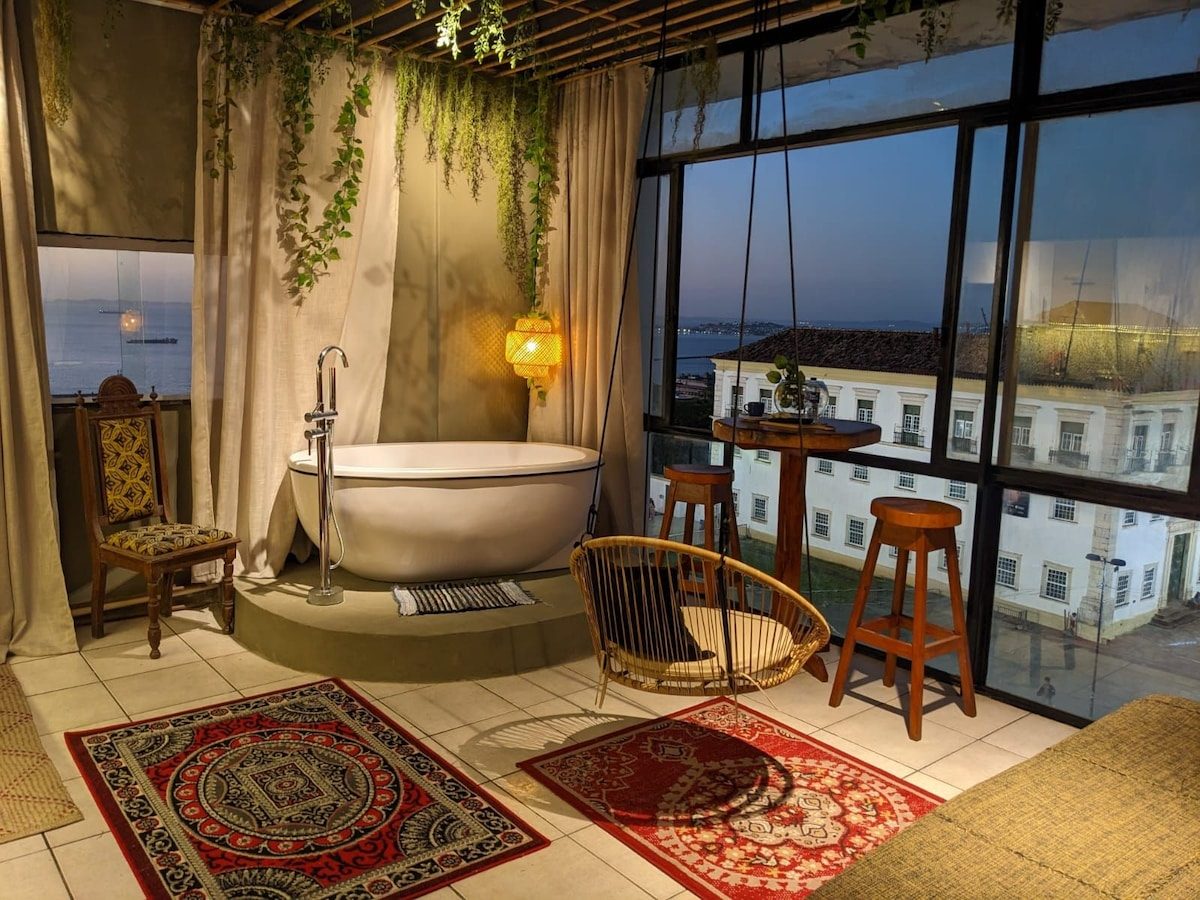 Freestanding white tub on a raised platform by the windows, bar stools and red rugs, colonial buildings outside