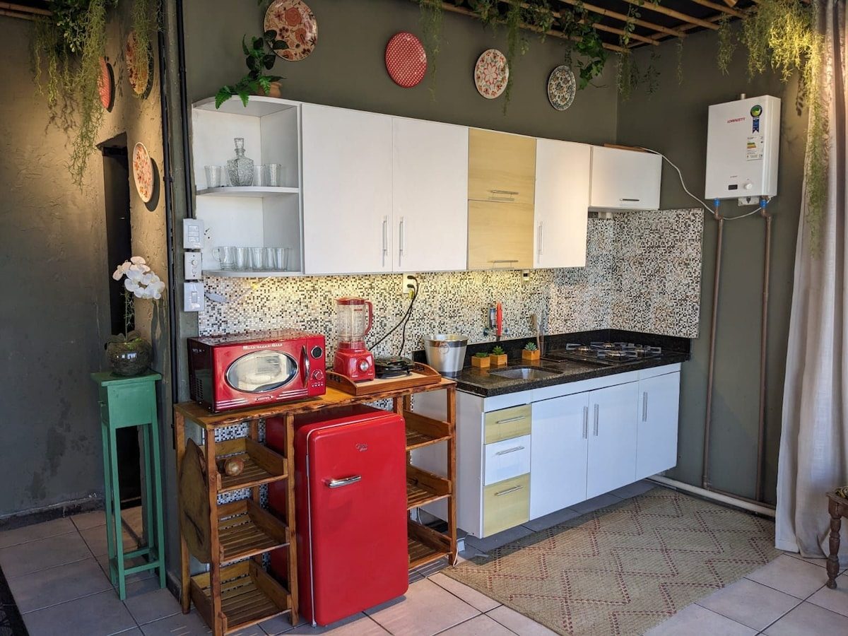 Small kitchen corner with a red retro fridge, a red microwave and wooden shelving under hanging plates