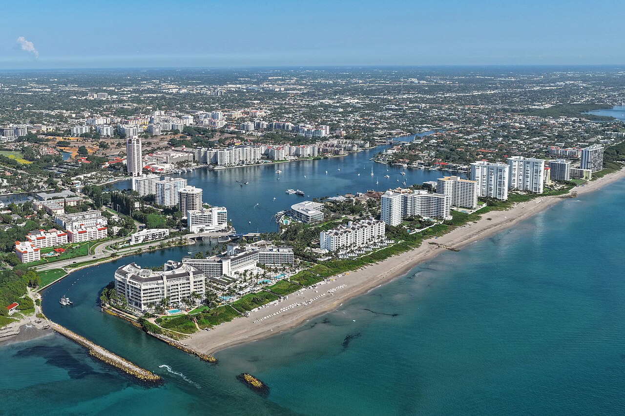 An aerial view of a coastal city with a large inlet, a lake, and numerous buildings along the beachfront.