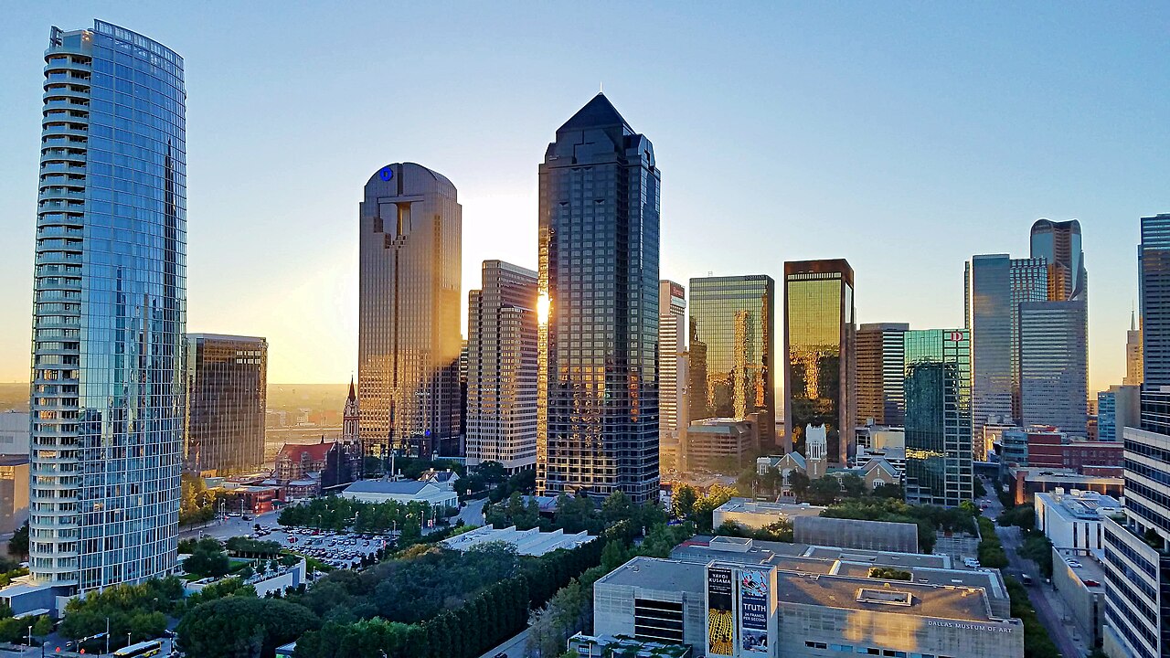A daytime view of the Dallas skyline with several tall buildings and a green area in the foreground.