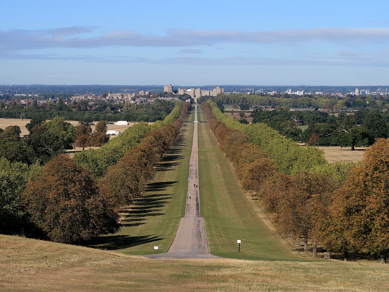 A long, straight avenue between double rows of trees turning to autumn colour, running to a castle on the horizon.