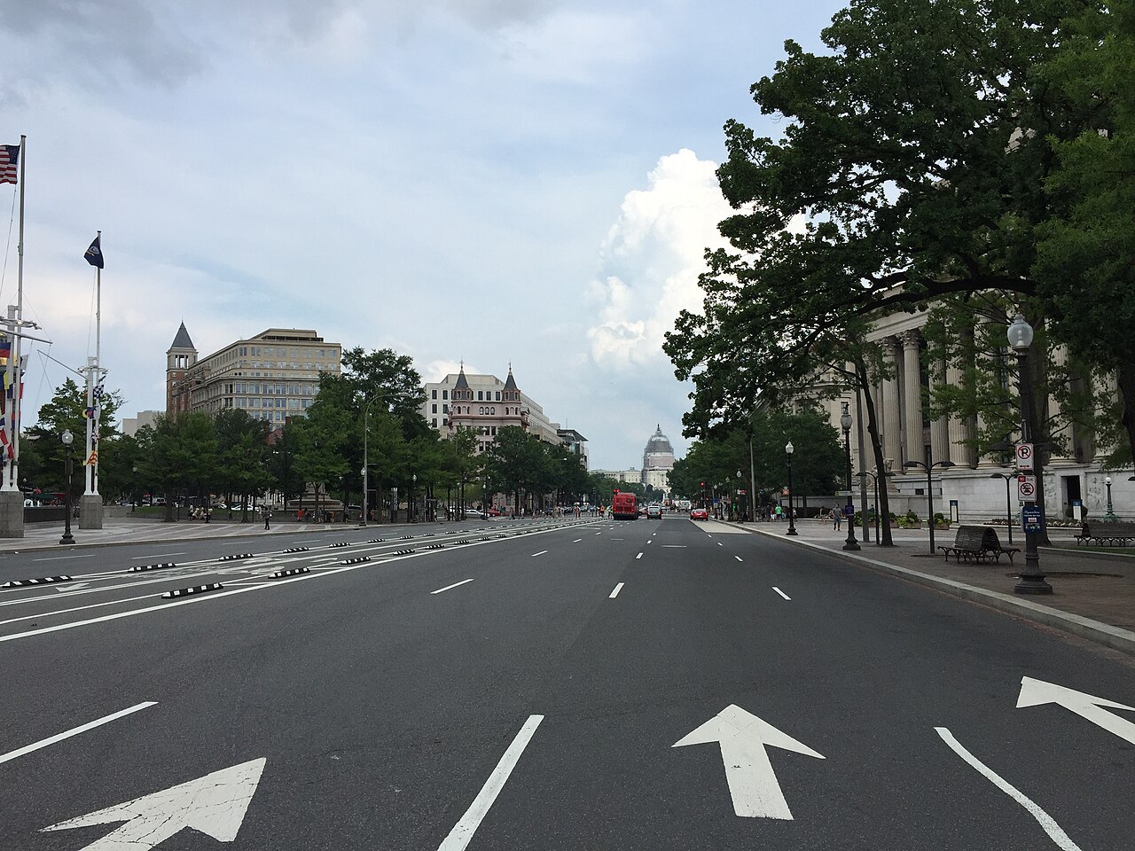 A broad, almost empty avenue with painted lane arrows, lined by trees and large stone buildings, leading to a domed building in the distance.
