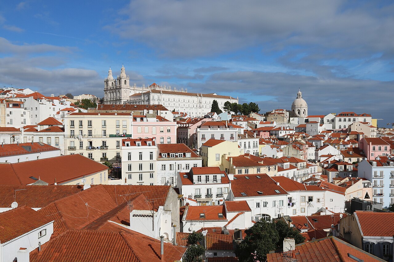 Red-tiled roofs and white houses climb a hillside toward a large white monastery and a domed church.