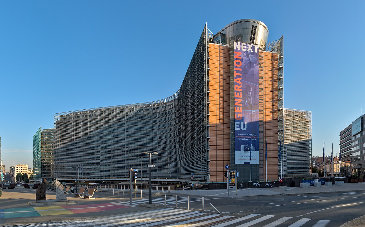 A curved glass and steel office block with a tall banner on its end wall, seen across an empty street crossing under a blue sky.