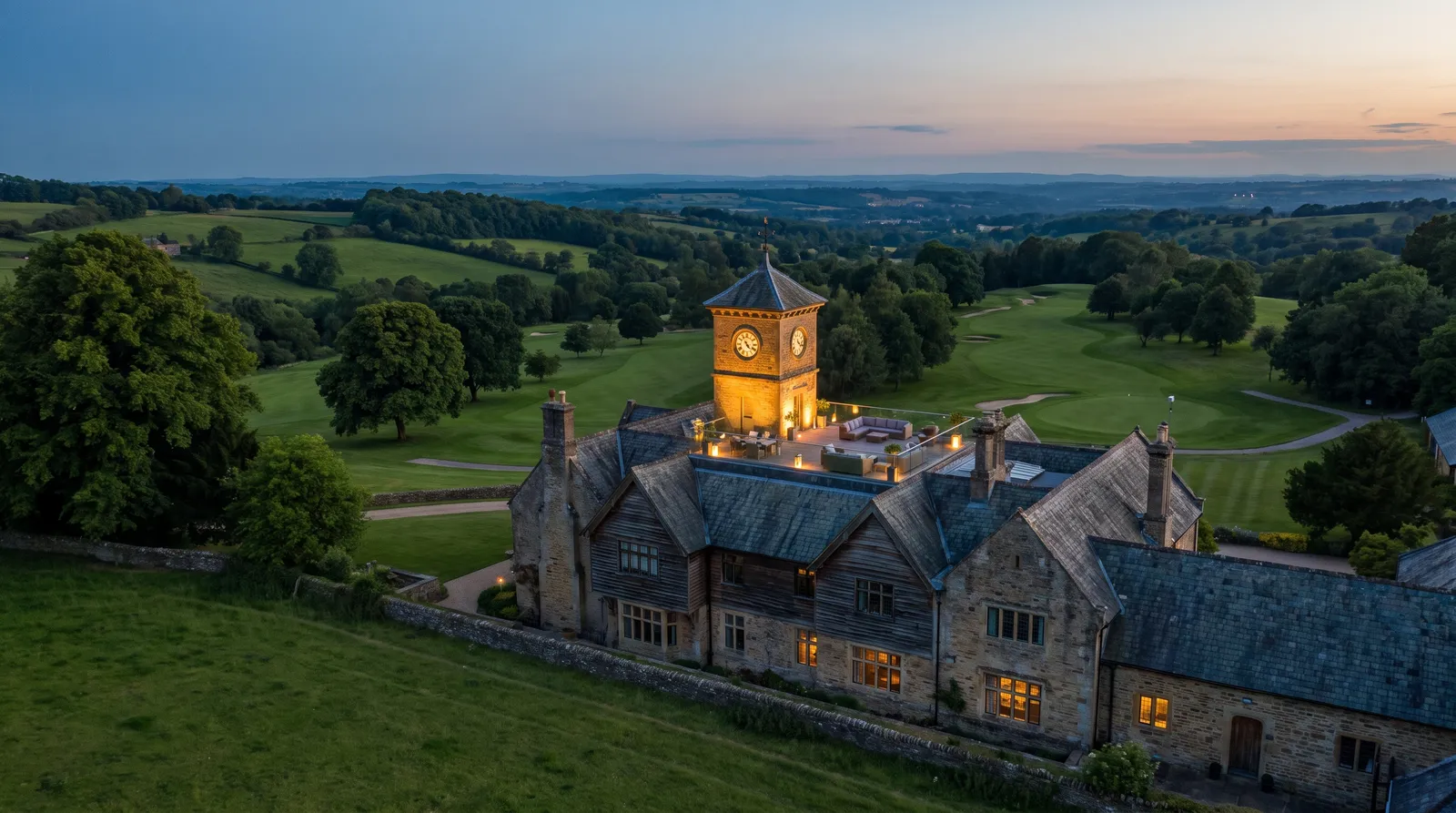 Wide view of a grand country estate hotel with an illuminated tower at dusk.