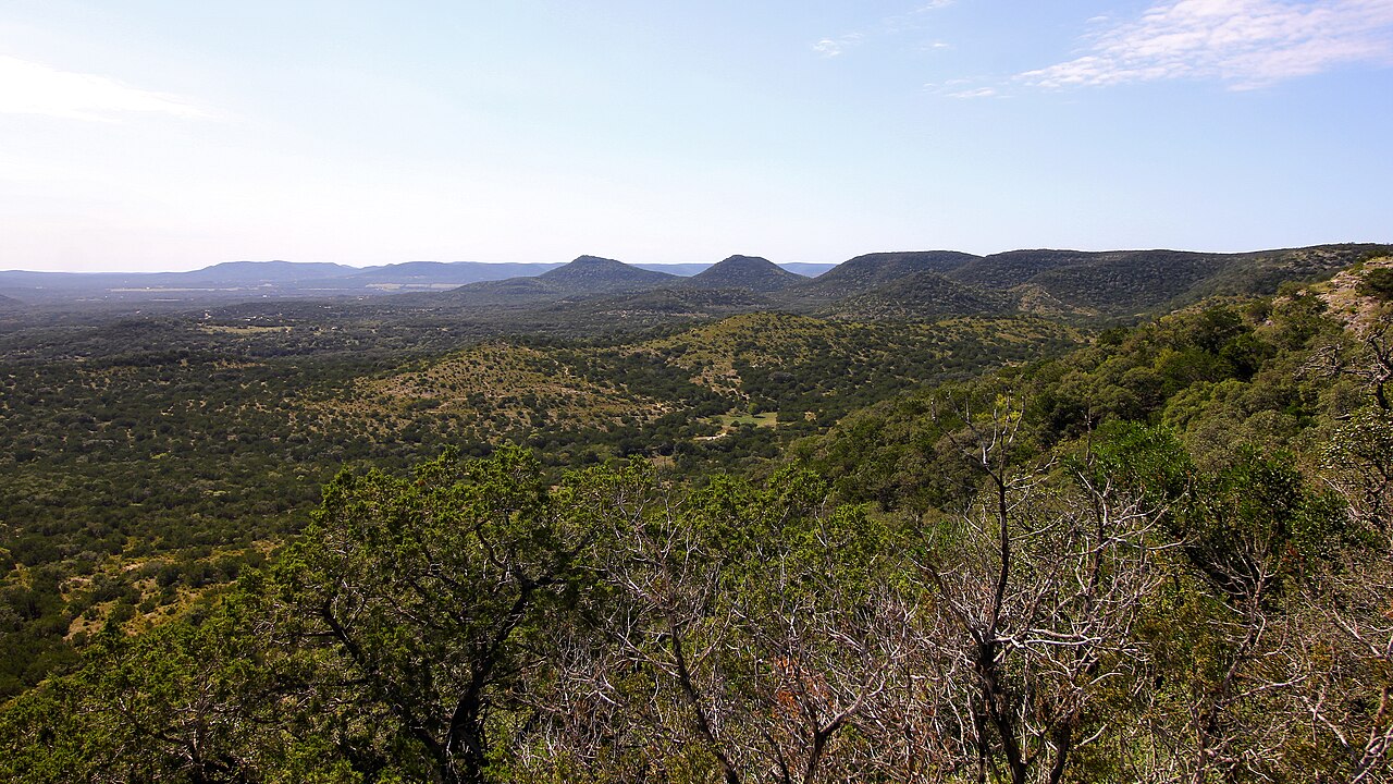 Scrub-covered hills roll away to a line of low blue ridges under a clear sky.