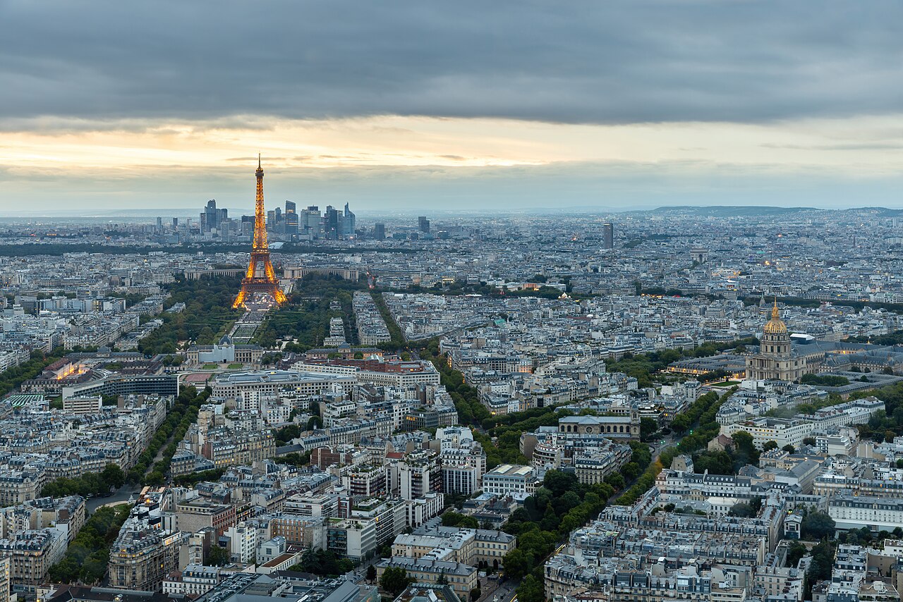 A panoramic view of a vast city skyline at dusk, with a lit Eiffel Tower and distant skyscrapers.