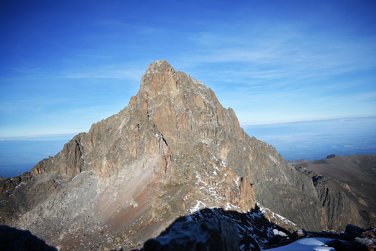 A sharp, rocky pyramid of a mountain peak rising above a sea of cloud under a deep blue sky.