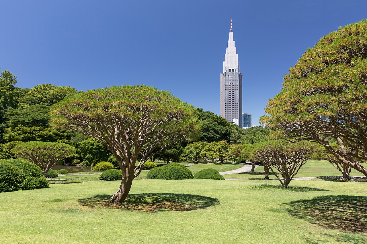 Sculpted pines and round clipped shrubs on a bright lawn, with a tall stepped tower rising behind the trees.