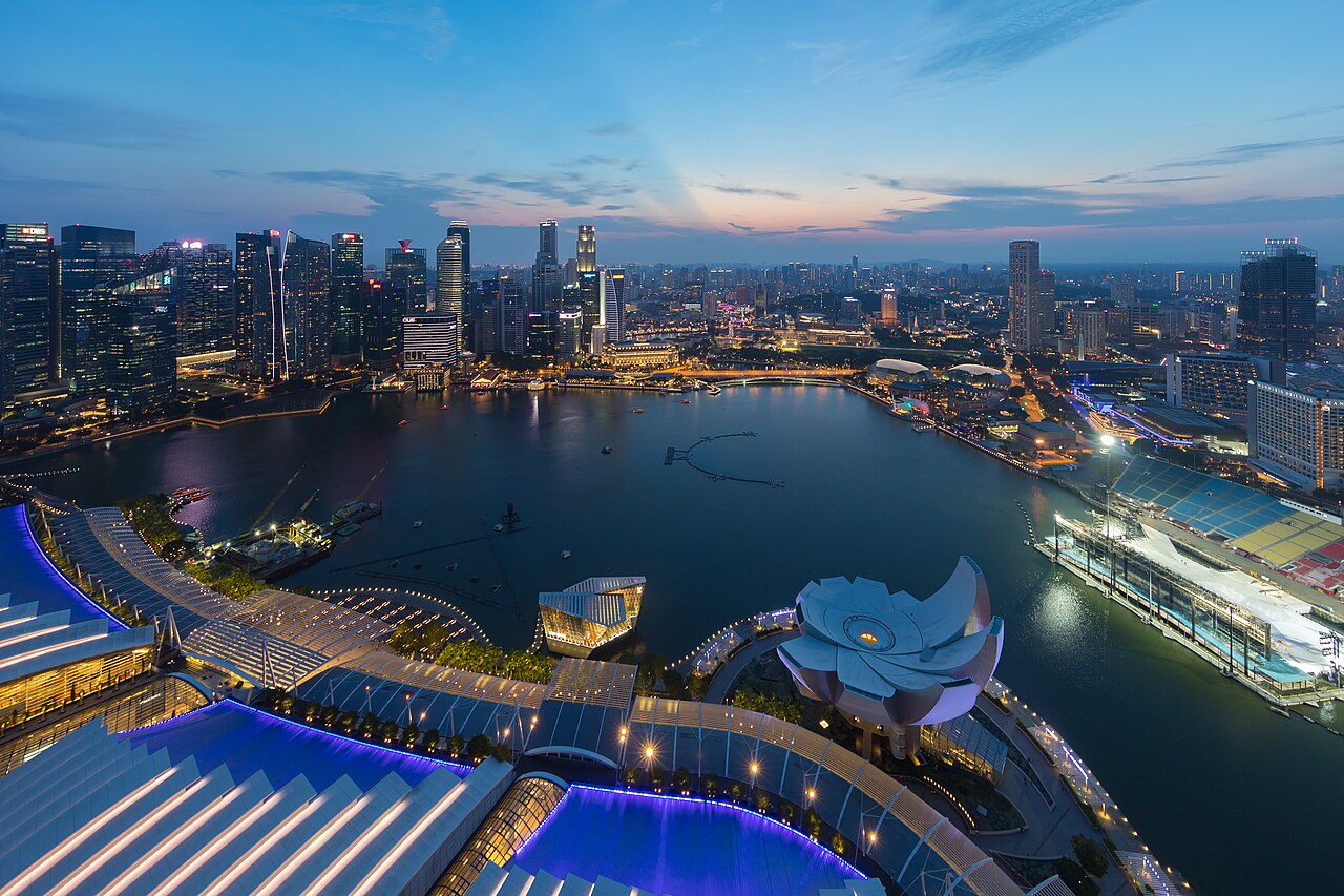 An aerial view of a city skyline at dusk, with numerous skyscrapers reflecting in a large body of water.
